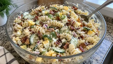 Big glass bowl of loaded bacon and egg pasta salad with rotini, cucumber, chopped egg, red onion and fresh dill