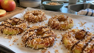 Finished caramel apple rings coated in toasted coconut on parchment, with a light chocolate drizzle