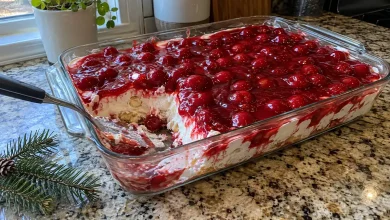 A 9x13 glass dish of cherries in the snow with a glossy cherry topping and a corner scooped out showing the white creamy angel food cake layer