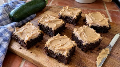 Chocolate peanut butter zucchini brownies with thick swirled peanut butter frosting on a walnut cutting board