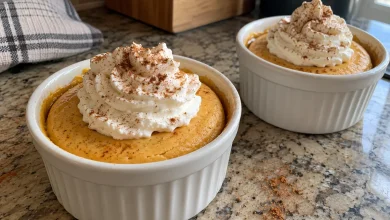 Two white ramekins of cottage cheese pumpkin cheesecake topped with whipped cream and a sprinkle of cinnamon