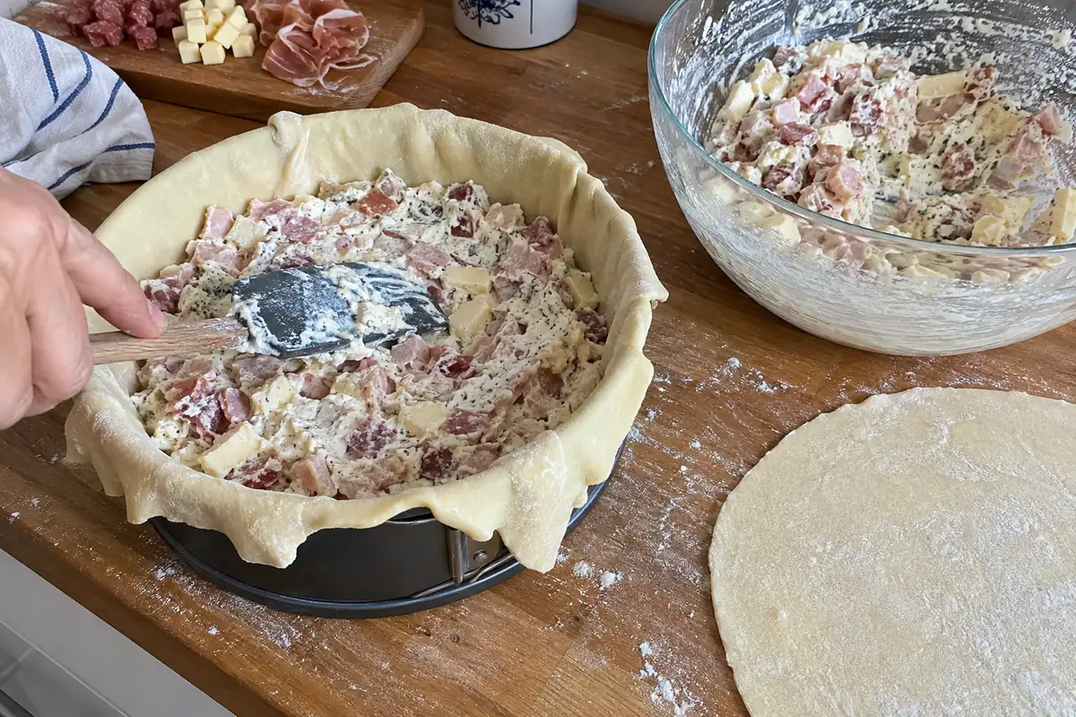 Spreading ricotta, meat and cheese filling into the dough-lined pan for Italian Easter pie