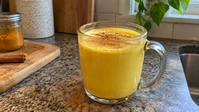 Glass mug of golden turmeric milk with a dusting of cinnamon on a kitchen counter