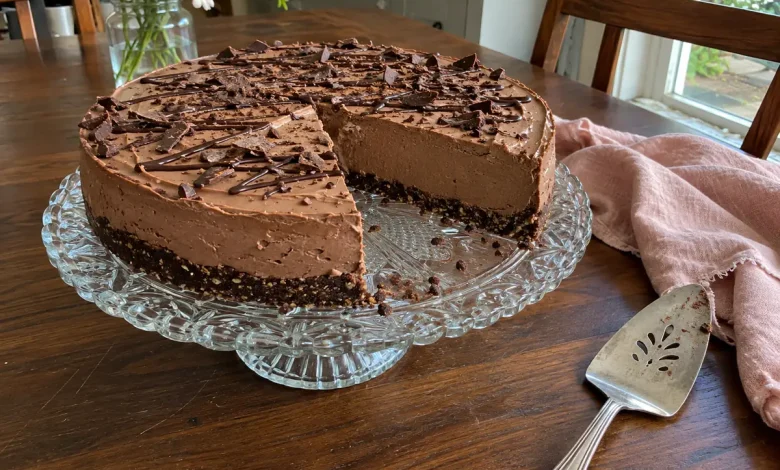 No-bake keto chocolate cheesecake with a chocolate drizzle and shavings on a vintage cake stand on a dark walnut table