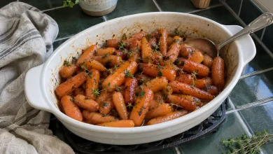 Slow cooker maple brown sugar glazed carrots in a serving dish, shiny with maple glaze and sprinkled with fresh parsley and thyme